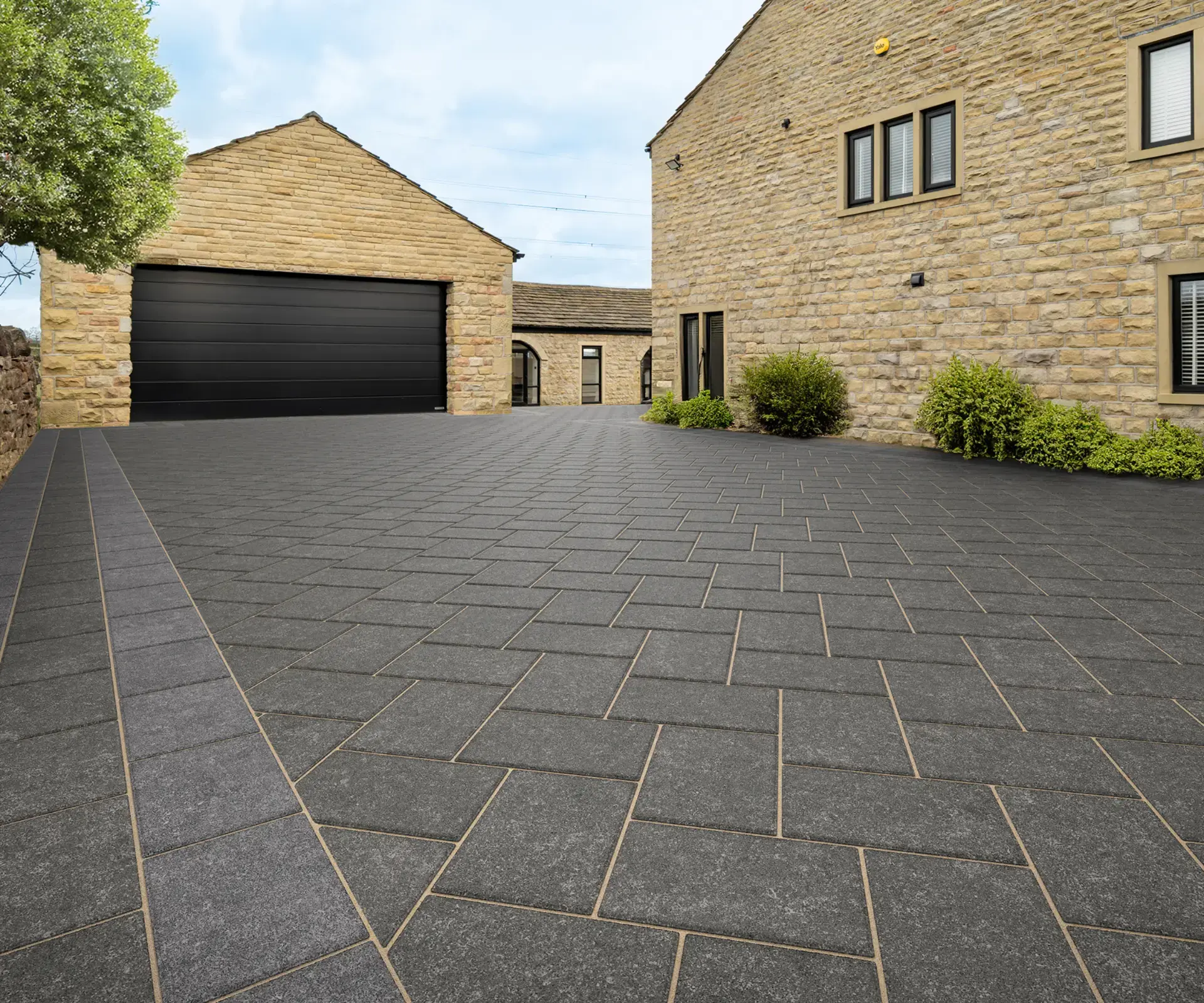 Dark granite block paved driveway sweeping up to a stone home with double garage